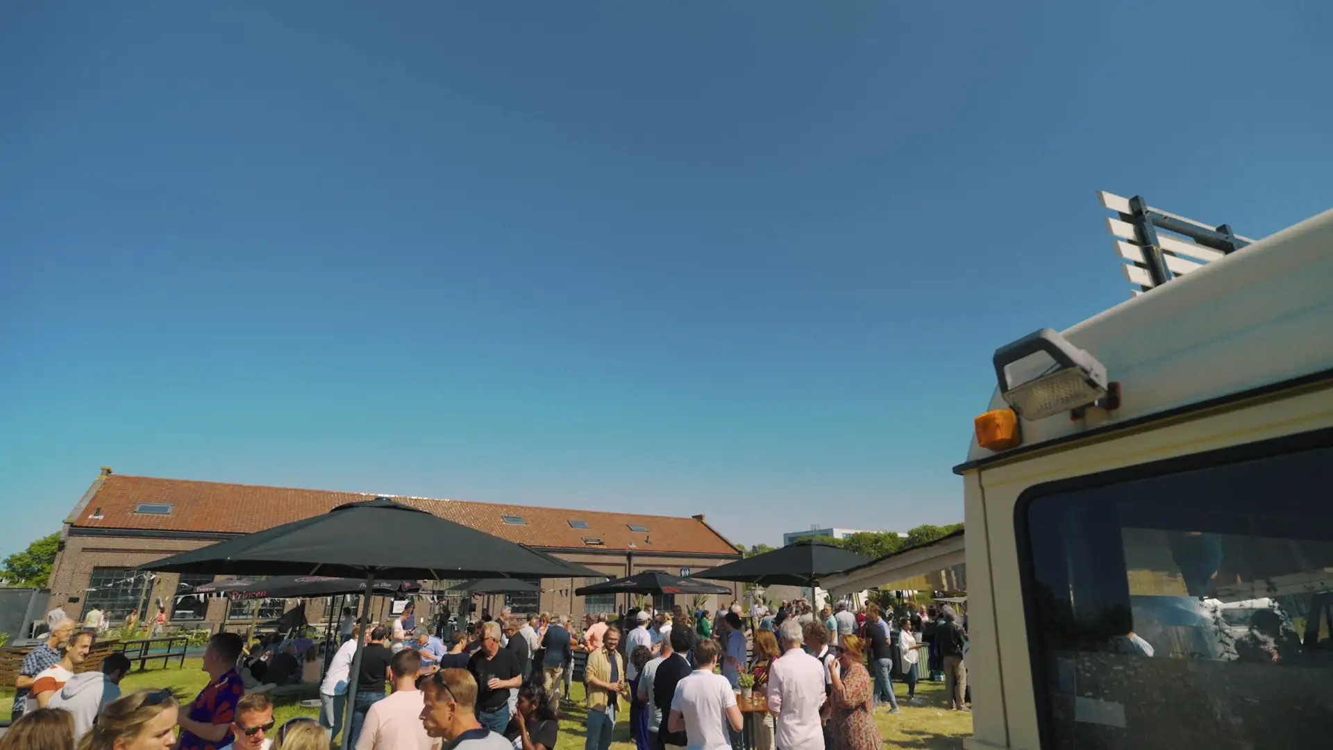 Verlichte reuzenrad en podium met band tijdens een openluchtfeest met groep mensen bij een industrieel terrein.