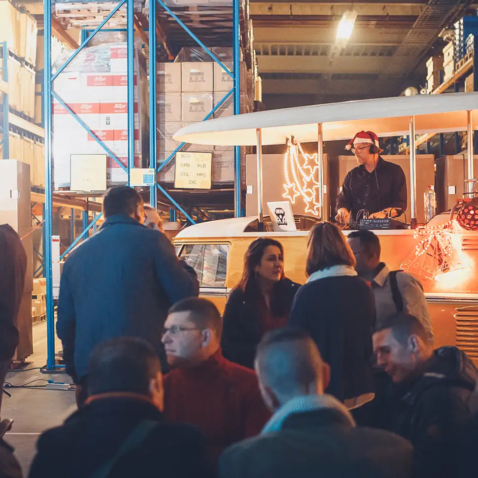 Mensen socialiseren bij een feestelijke DJ-stand in een magazijn met kerstverlichting en een DJ met een kerstmanmuts.