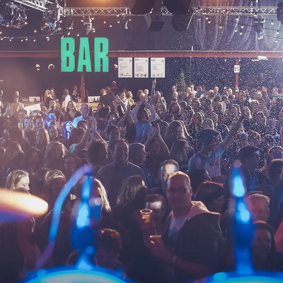 Grote menigte mensen die feestvieren in een drukke bar met verlichting en confetti in de lucht.