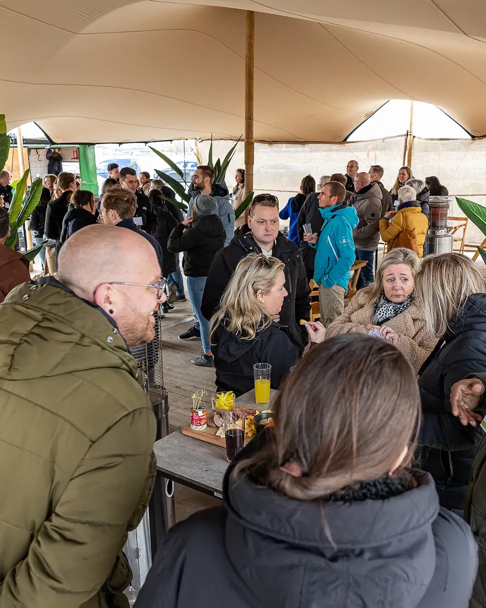 Mensen in winterkleding praten en drinken onder een grote tent tijdens een bijeenkomst.