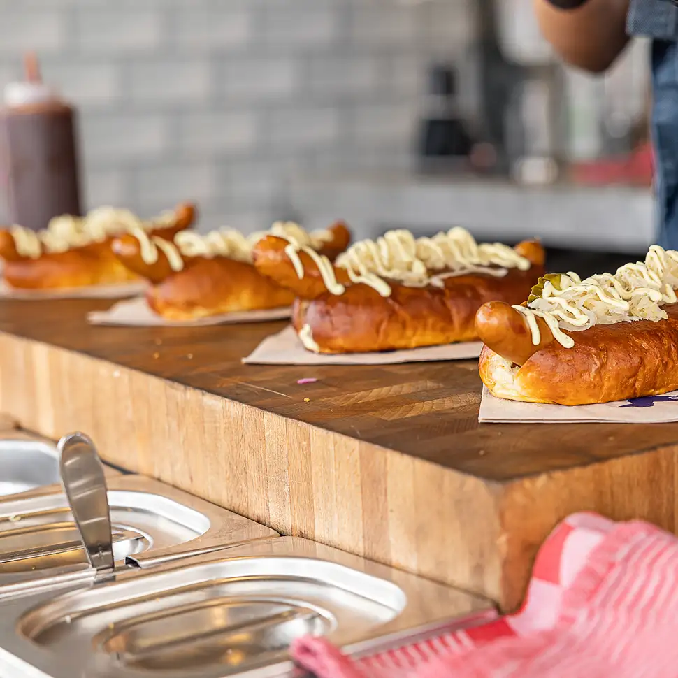 Vier broodjes worst met een royale hoeveelheid mayonaise erop, geplaatst op een houten plank in een eetgelegenheid.