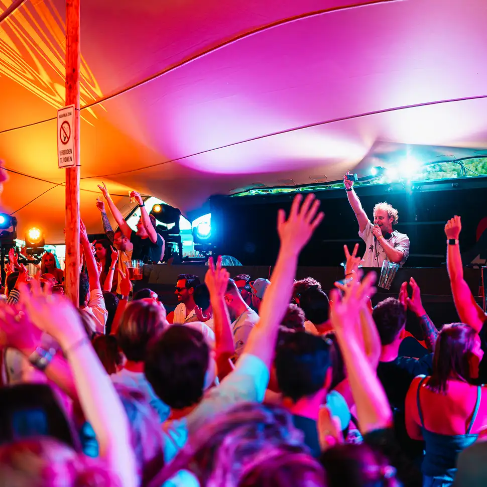 Houten plank met diverse hapjes: plakjes kaas en vleeswaren, een blikje olijven, een metalen schep met gemengde noten en gedroogd fruit, en een klein kommetje met groene olijven.