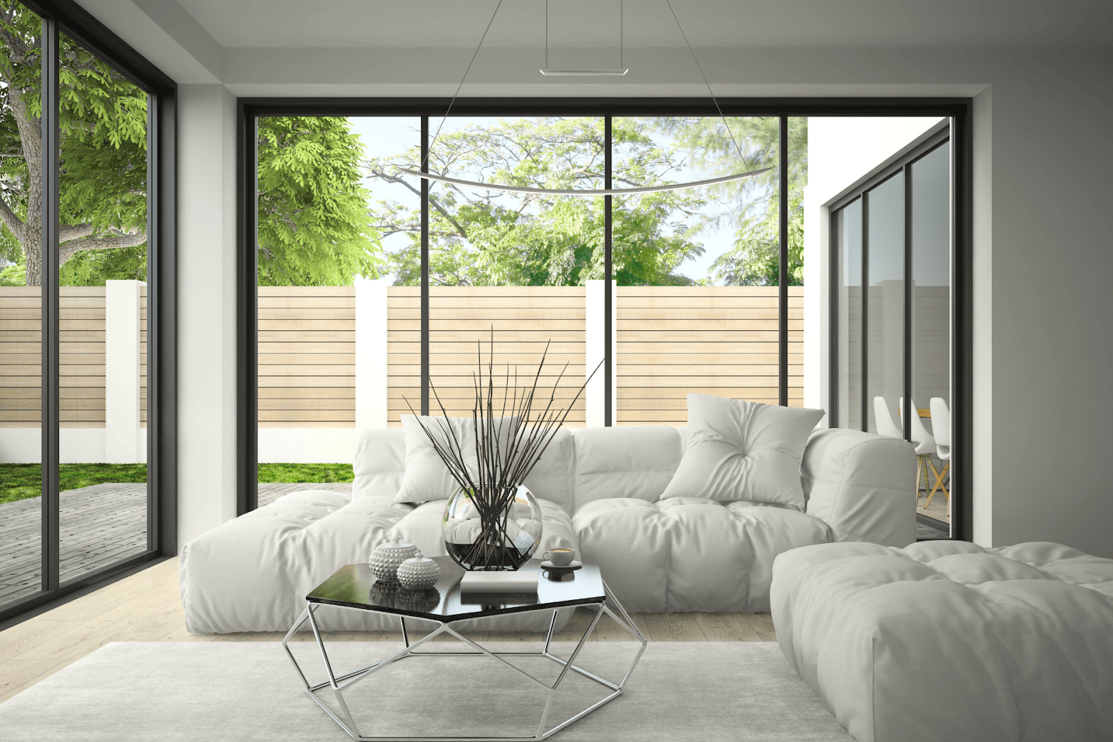 Bright, modern living room with large floor-to-ceiling black-framed windows overlooking a green backyard, featuring a plush white sectional sofa and a minimalist coffee table.