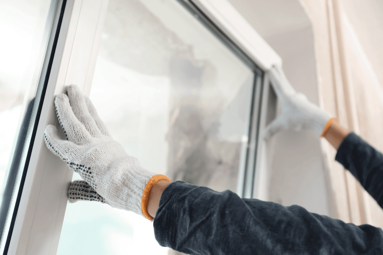 Worker wearing white safety gloves installs a new double-pane window into a white frame.