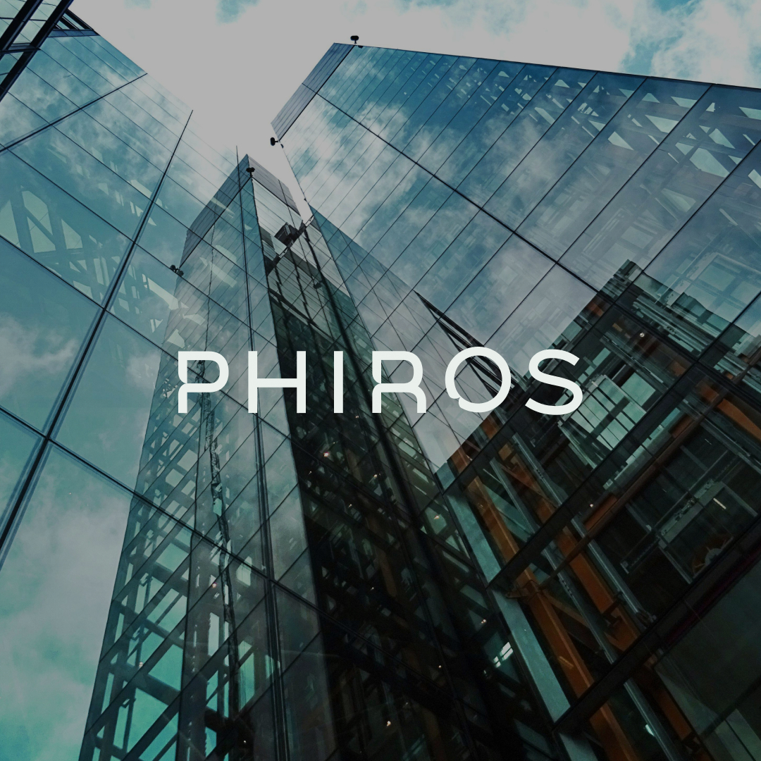 Low-angle view of modern glass skyscrapers reflecting the sky with the word PHIROS overlayed in white letters.