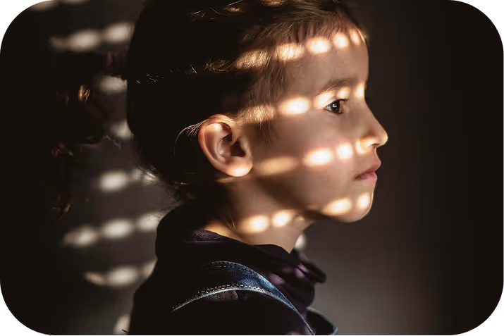 Little girl reading a large illustrated book in a dimly lit room, with warm light and holiday decorations behind her.