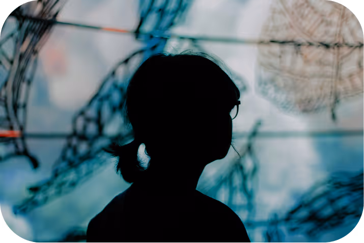 Little girl reading a large illustrated book in a dimly lit room, with warm light and holiday decorations behind her.