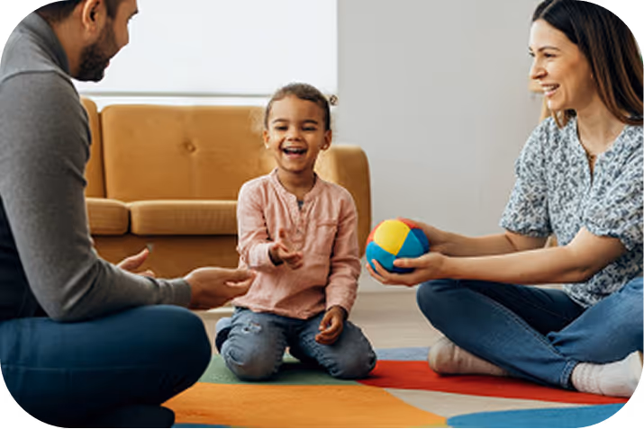 Little girl reading a large illustrated book in a dimly lit room, with warm light and holiday decorations behind her.