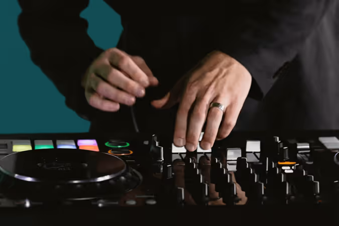 Close-up of a DJ's hands adjusting controls on a mixer with colorful buttons and knobs.