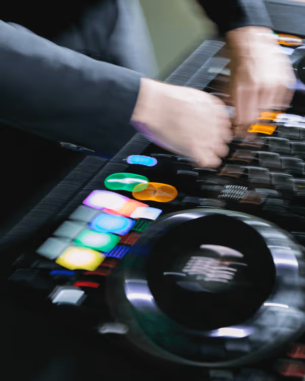 Blurred hands of a DJ manipulating a colorful mixing console with illuminated buttons and a large jog wheel.
