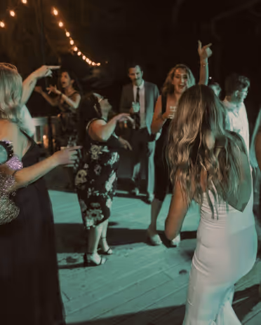 Group of people dancing and socializing at an outdoor nighttime party with string lights overhead.