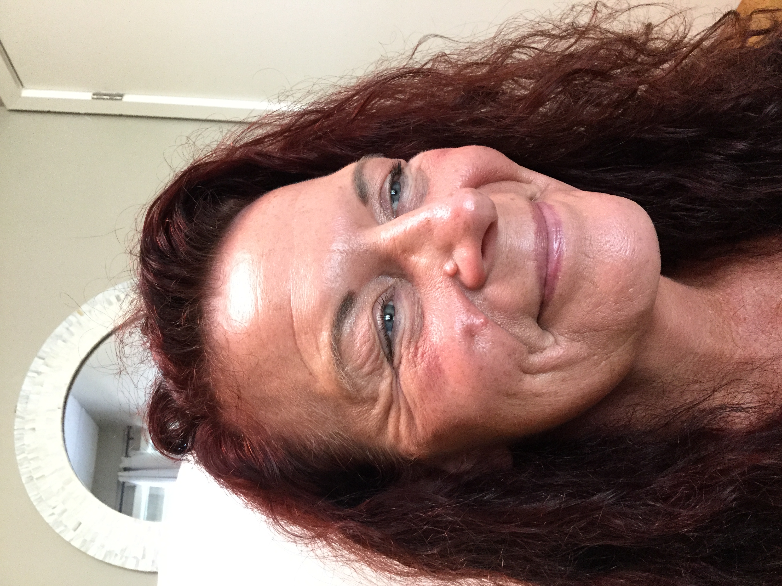 Smiling middle-aged woman with red curly hair, visible wrinkles around her eyes and cheeks.