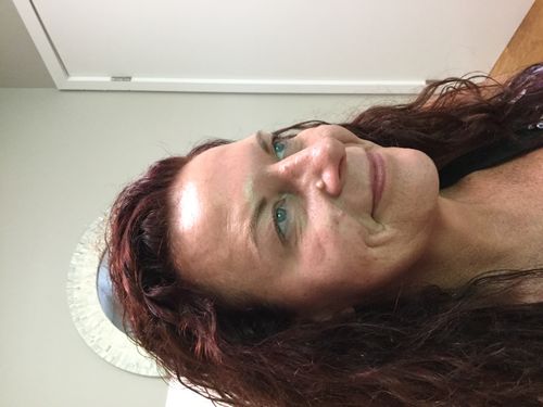 Side profile of a woman with curly red hair, blue eyes, and clear skin smiling softly indoors.