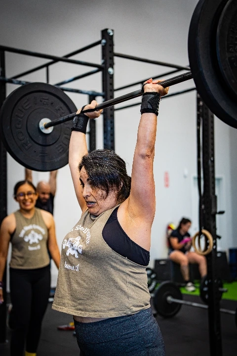 Woman performing an overhead barbell lift during a CrossFit workout.