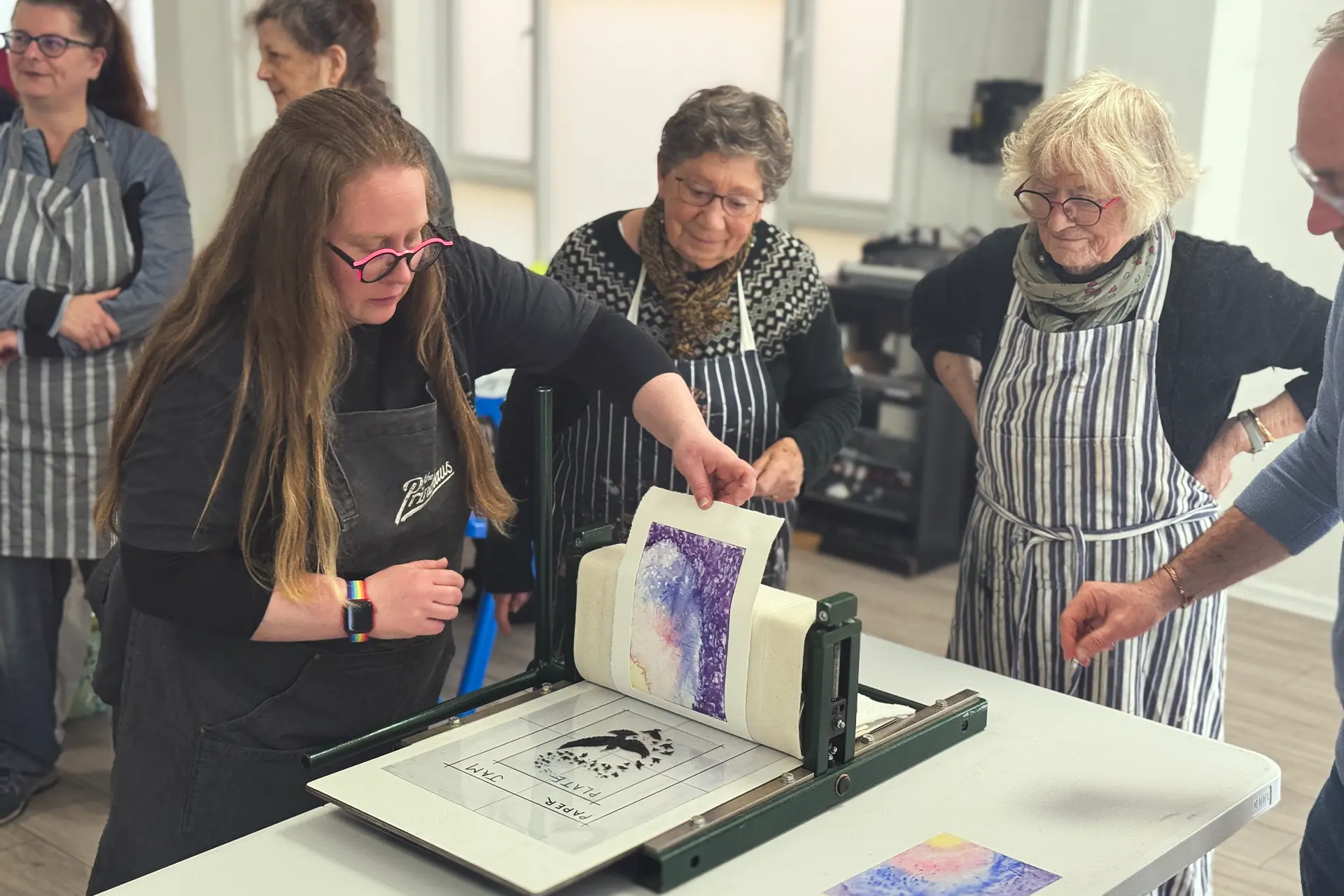 Workshop participants in aprons pulling a purple monotype print through a press
