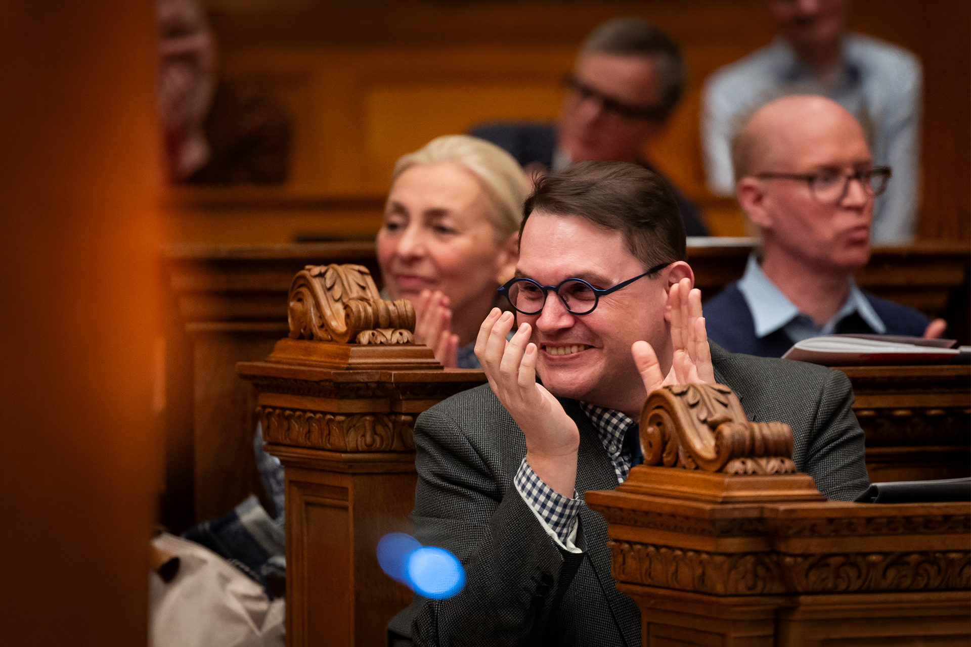 Composer Paul Mealor applauding at a JAM concert, seated among carved wooden stalls.