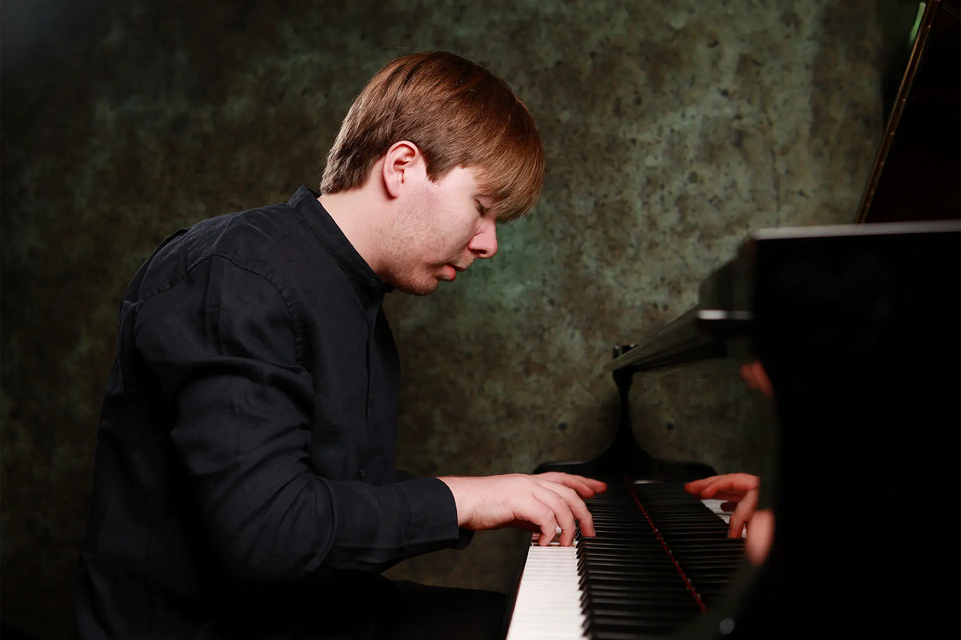 Pianist Thomas Kelly performs at the JAM Festival at the grand piano in profile, warm moody light.