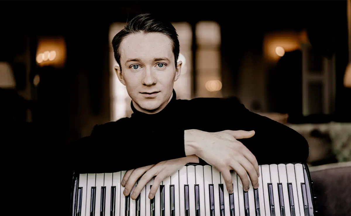 Ryan Corbett with his accordion, leaning against iron railings on a London street.