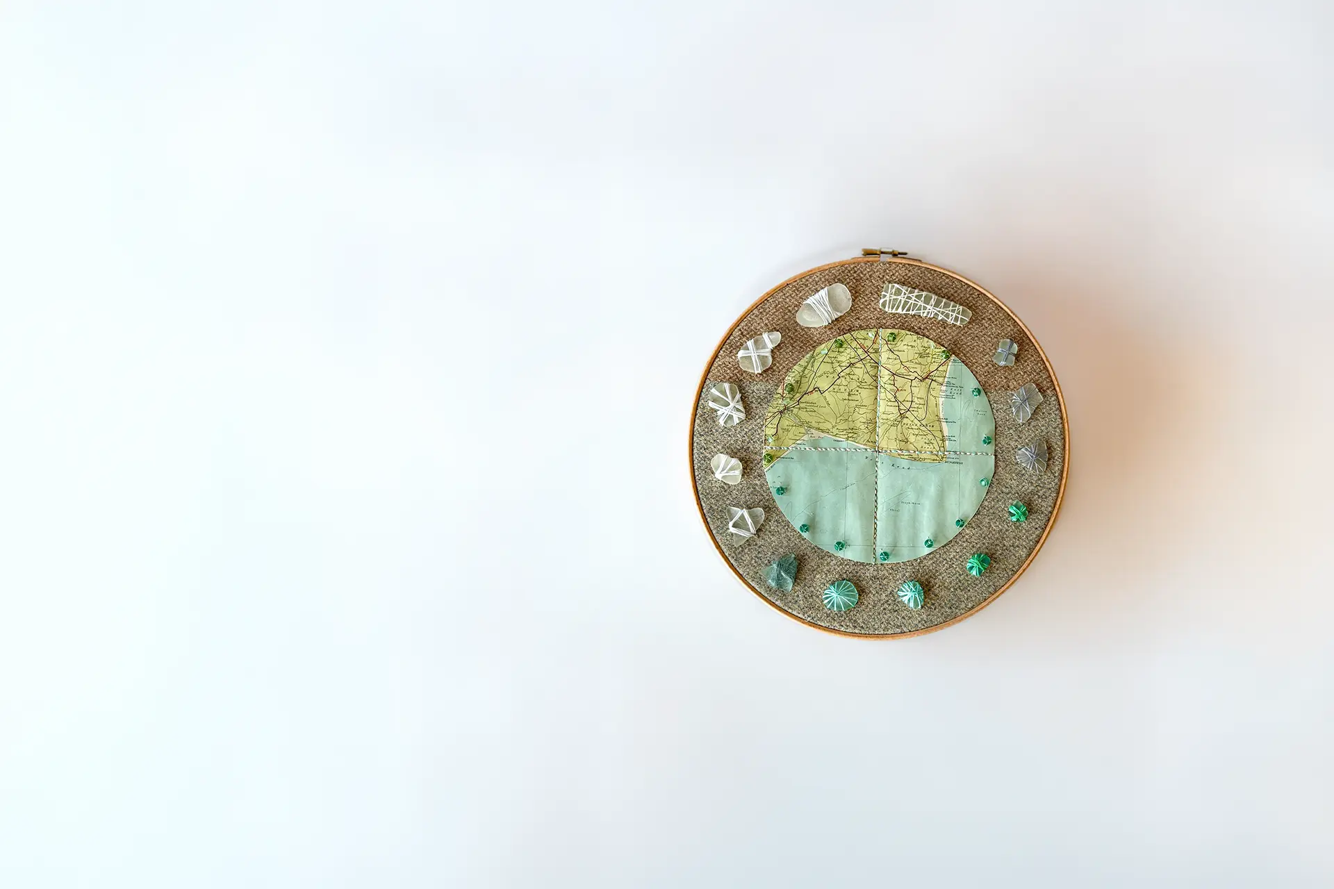 An embroidery-hoop collage of a Romney Marsh map framed by thread-wrapped sea glass and beads.