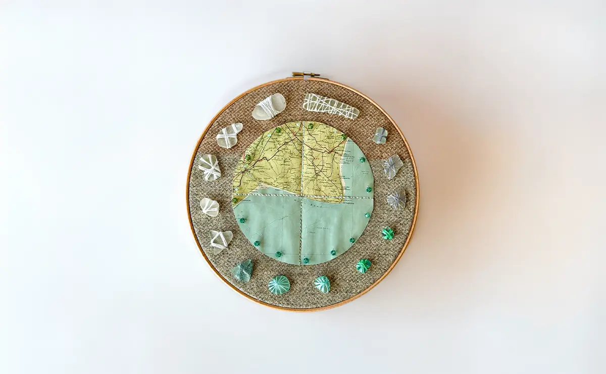 An embroidery-hoop collage of a Romney Marsh map framed by thread-wrapped sea glass and beads.