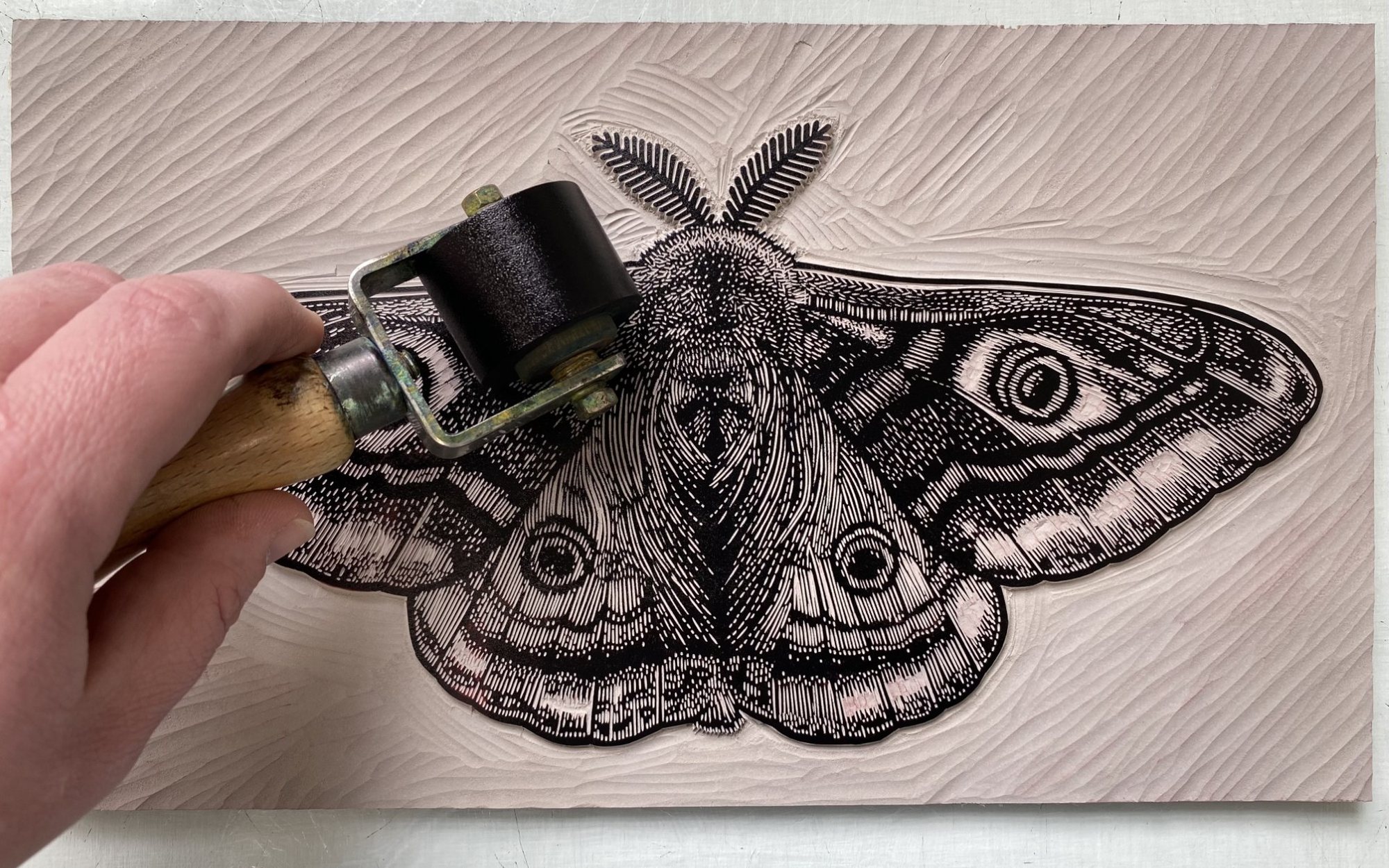 A hand inking a lino block cut with a moth design