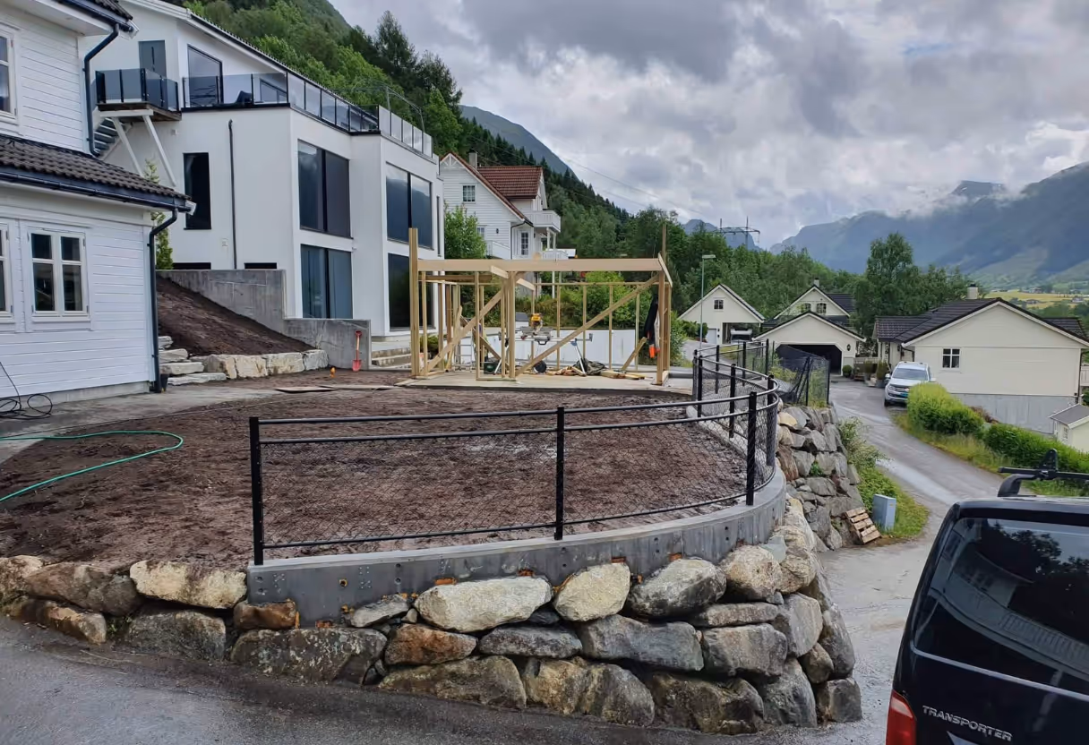 Steinmursgjerde med svart metallrekkverk rundt en hage i oppussingsområdet ved hus i fjellområdet.
