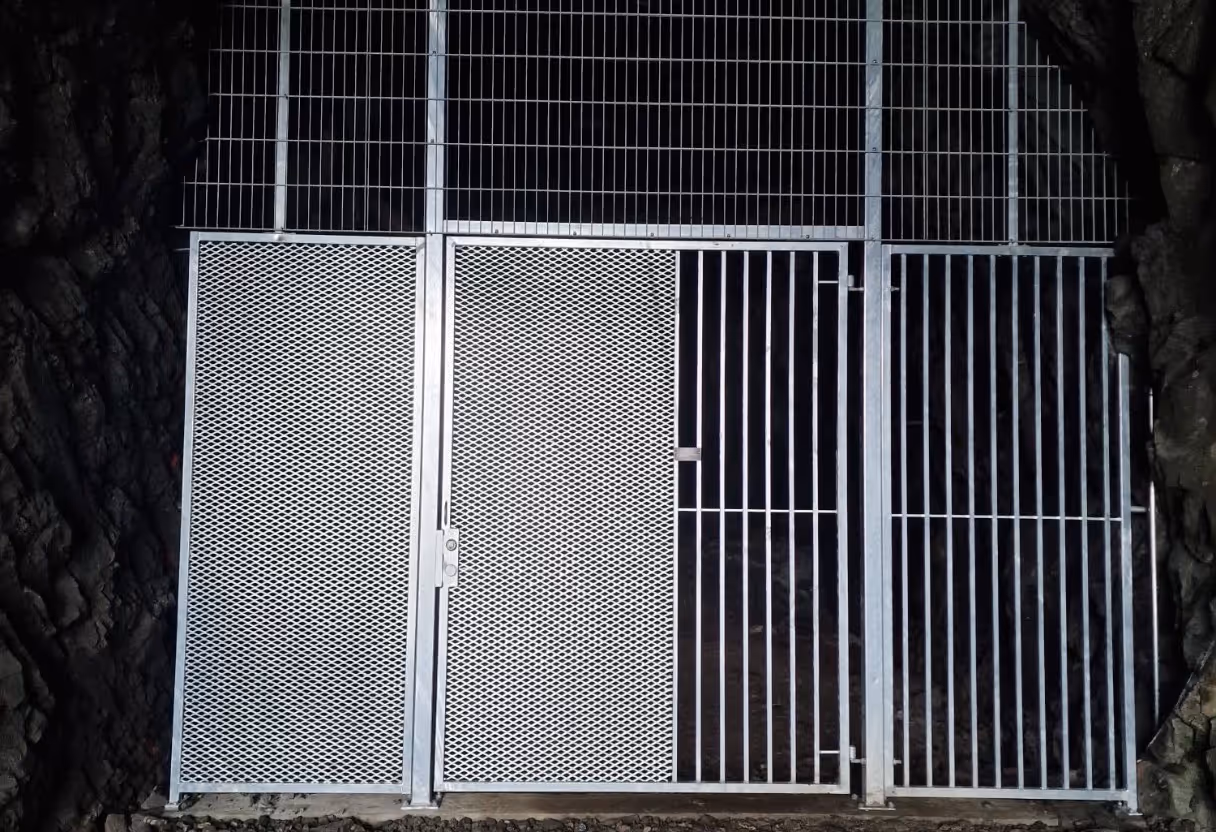 Metal secure gate with a locked door, set in a rocky cave entrance.