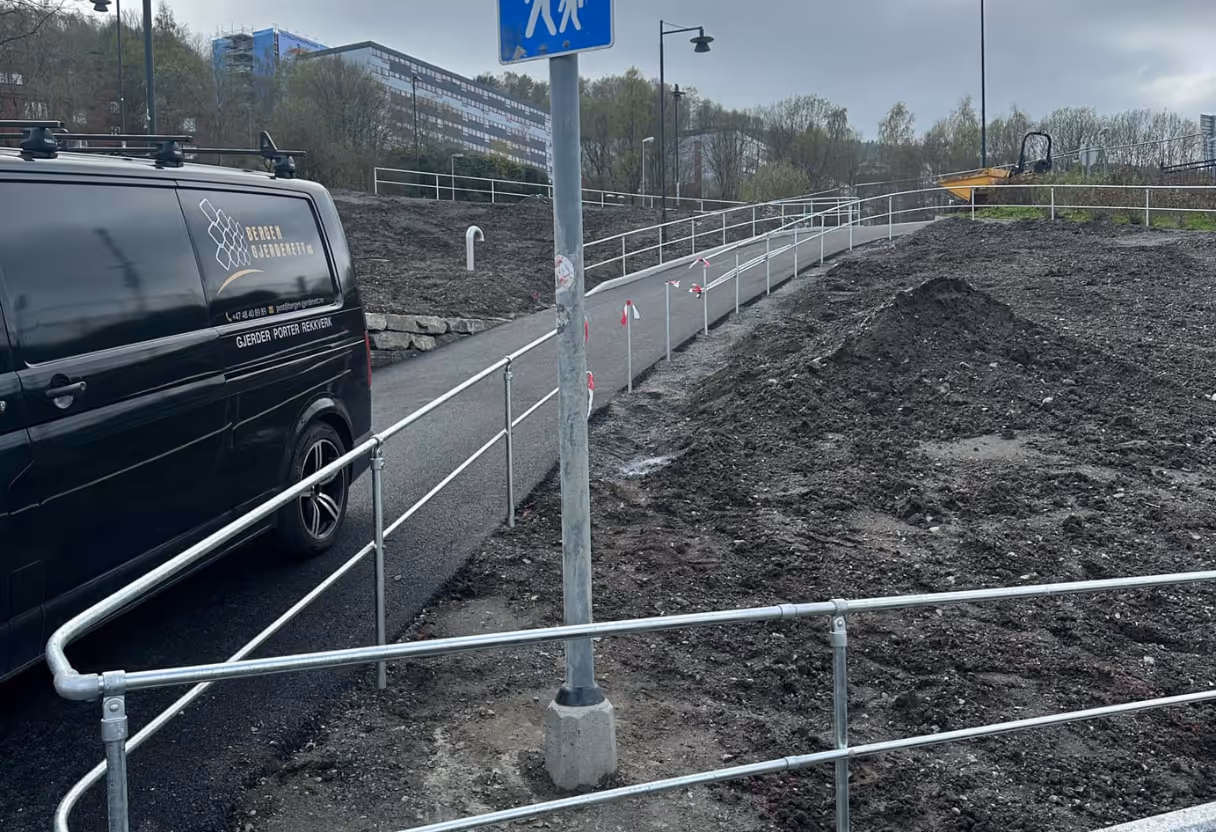 Rullestolrampe med nybygd metallrekkverk langs asfaltsti ved en byggeplass.