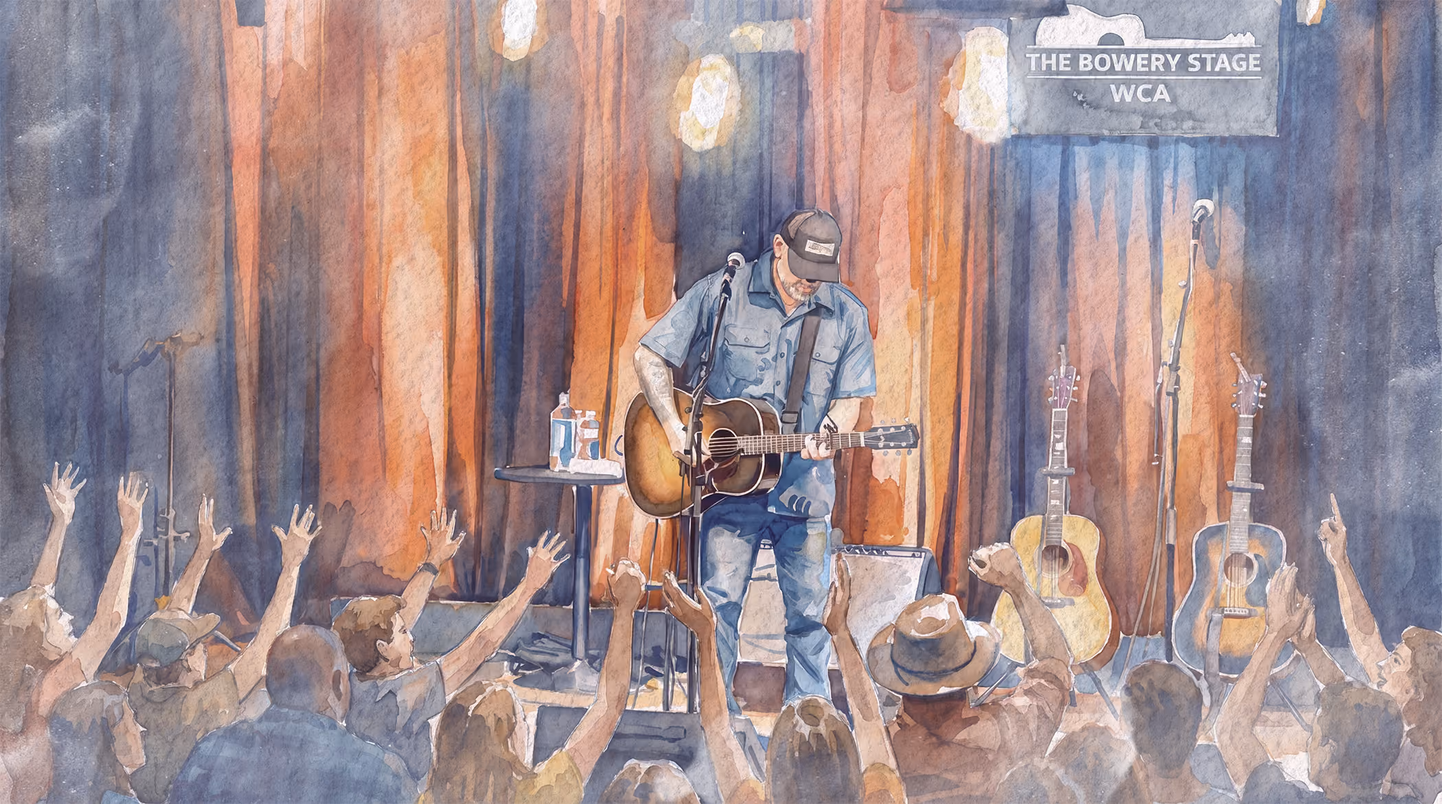 Man playing guitar on stage at The Bowery Stage with an audience raising their hands.