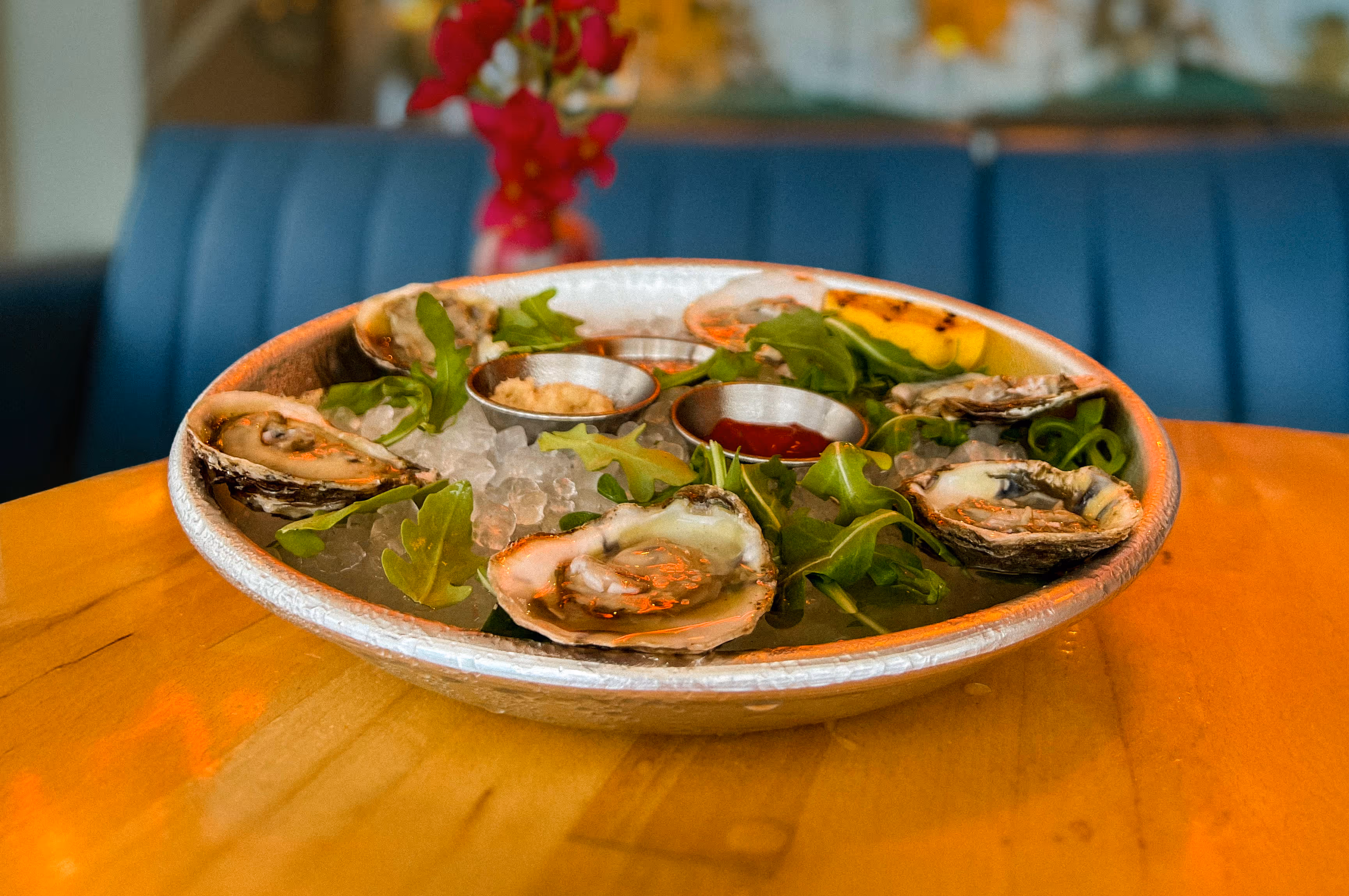 Fresh raw oysters on the half shell served on ice with arugula, lemon, and cocktail sauces, a seafood appetizer from Osteria del Mar Miami Beach.