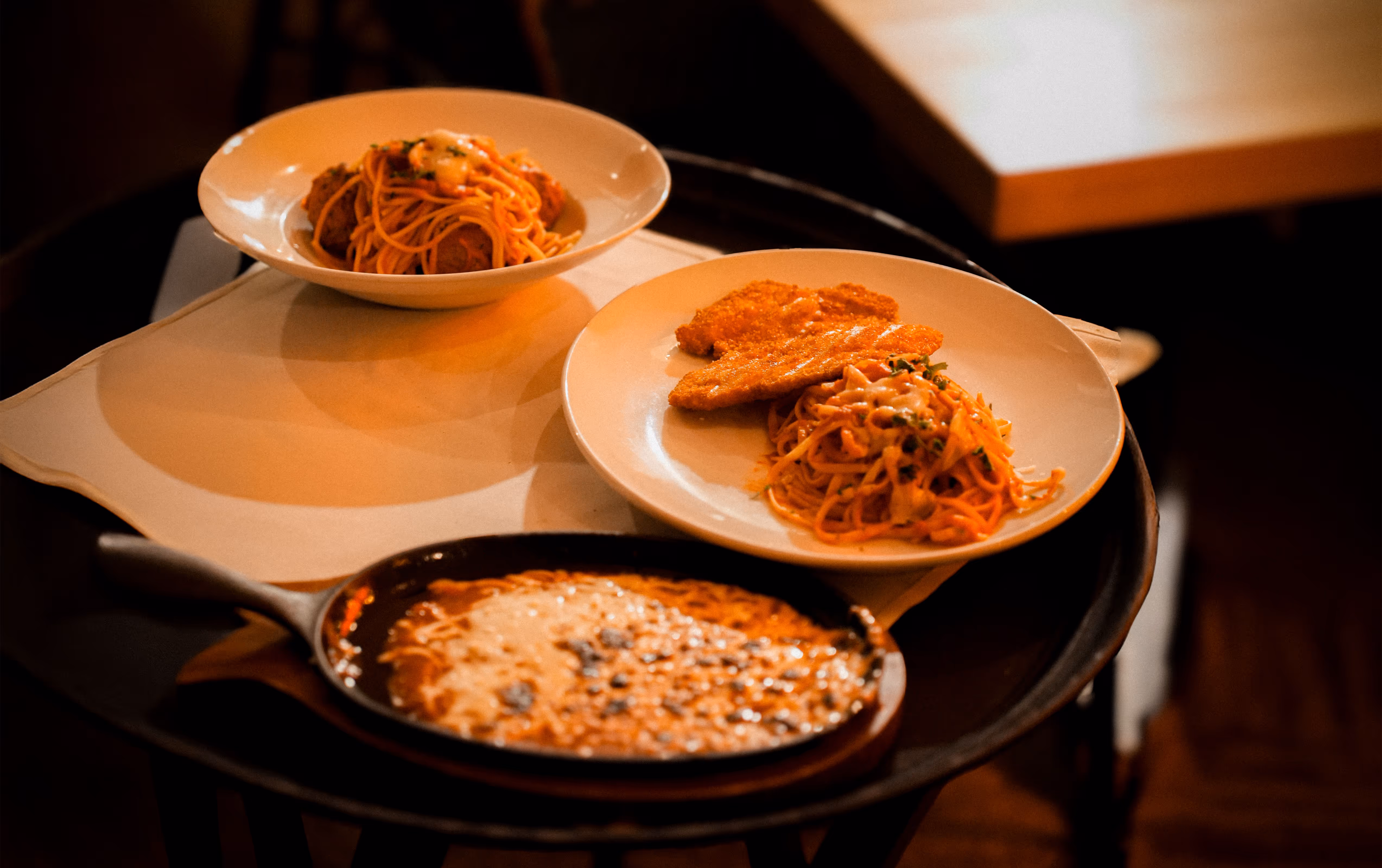 Italian dining scene at Osteria del Mar Miami Beach featuring spaghetti with meatballs, chicken parmesan and spaghetti, and a skillet of baked pasta or lasagna with melted cheese.