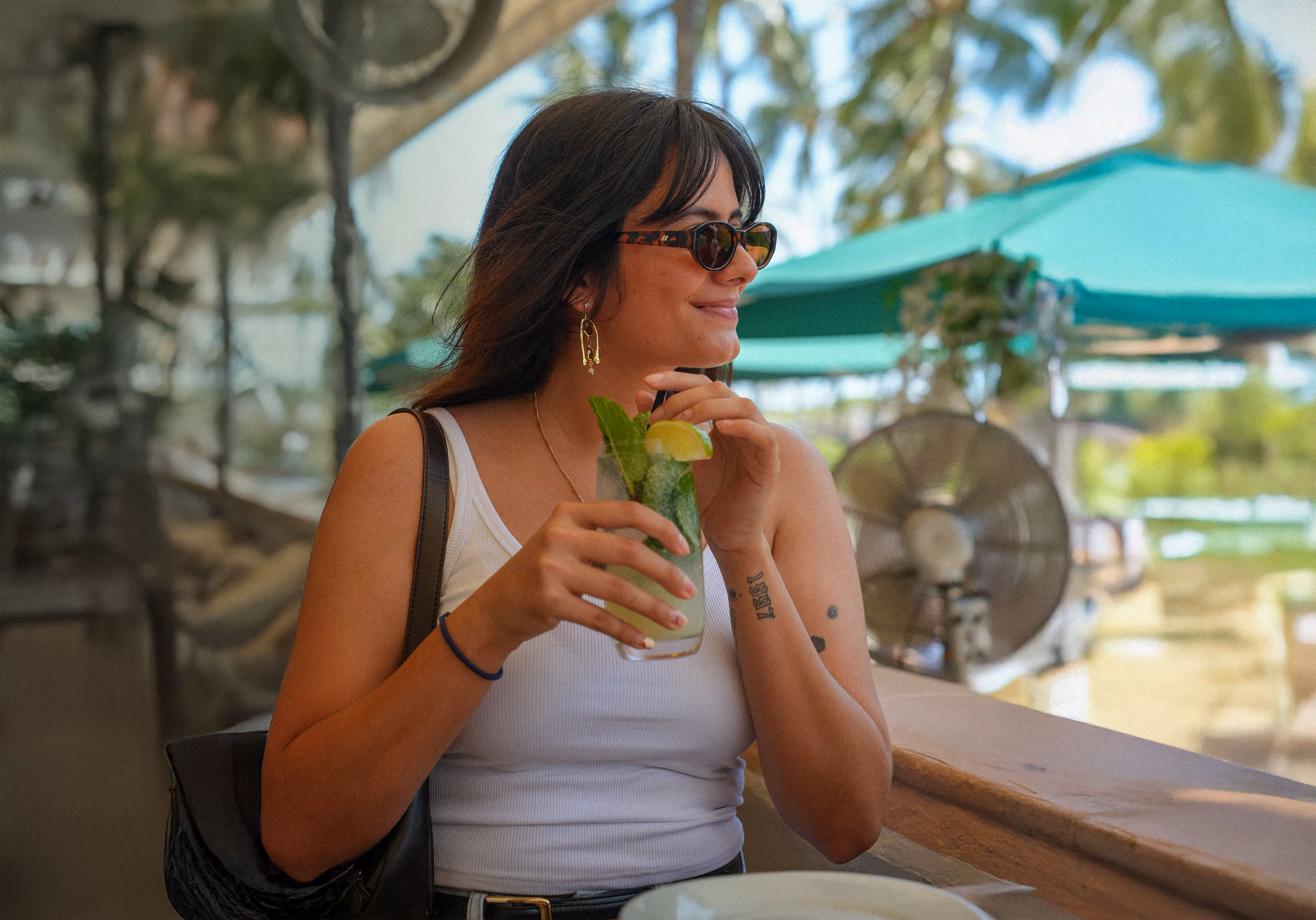 Happy woman in sunglasses enjoying a fresh mojito cocktail with mint and lime on a sunny terrace at Osteria del Mar Miami Beach.