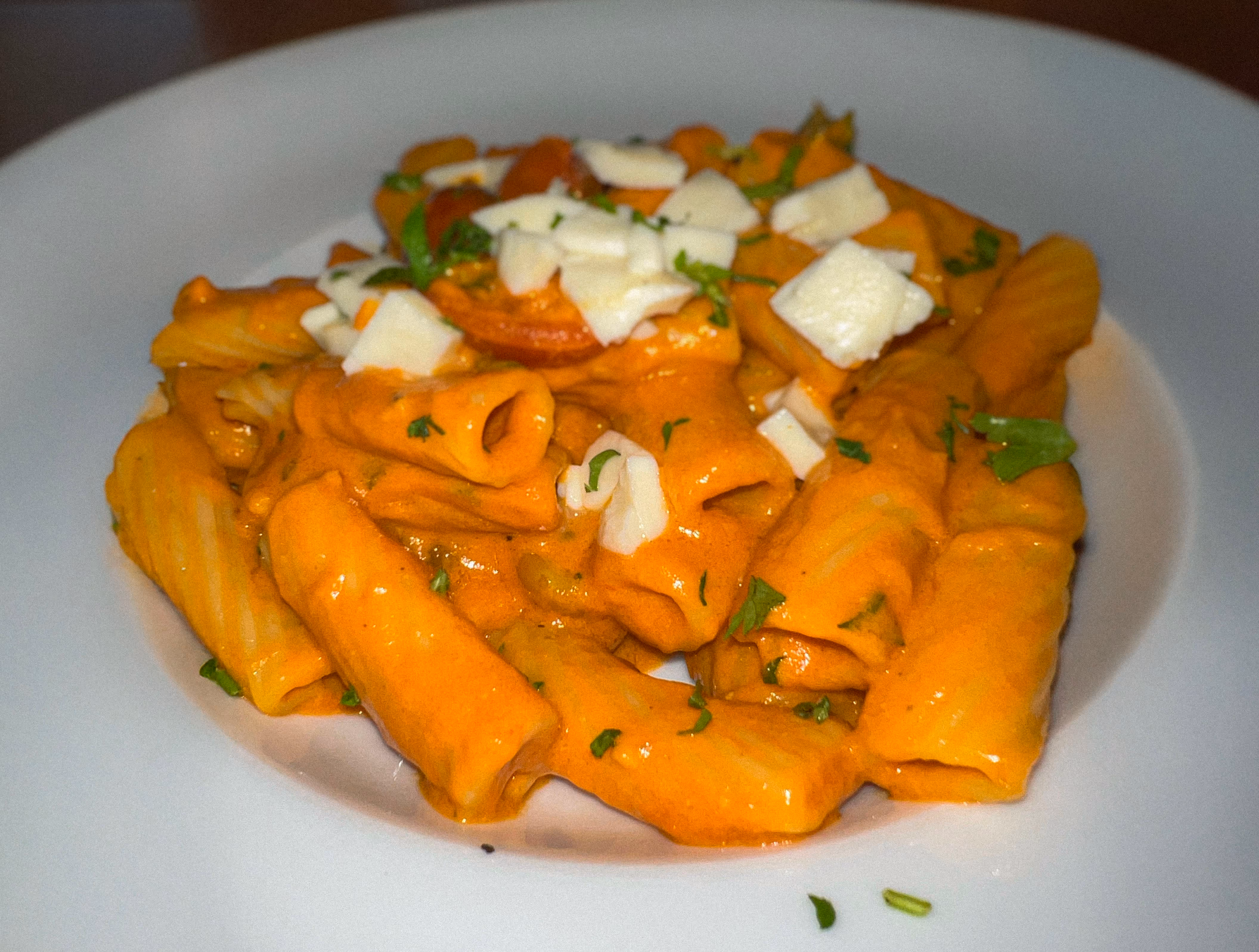 A plate of creamy rigatoni pasta with a rich orange sauce, topped with shaved or cubed fresh mozzarella cheese and parsley, served at Osteria del Mar.