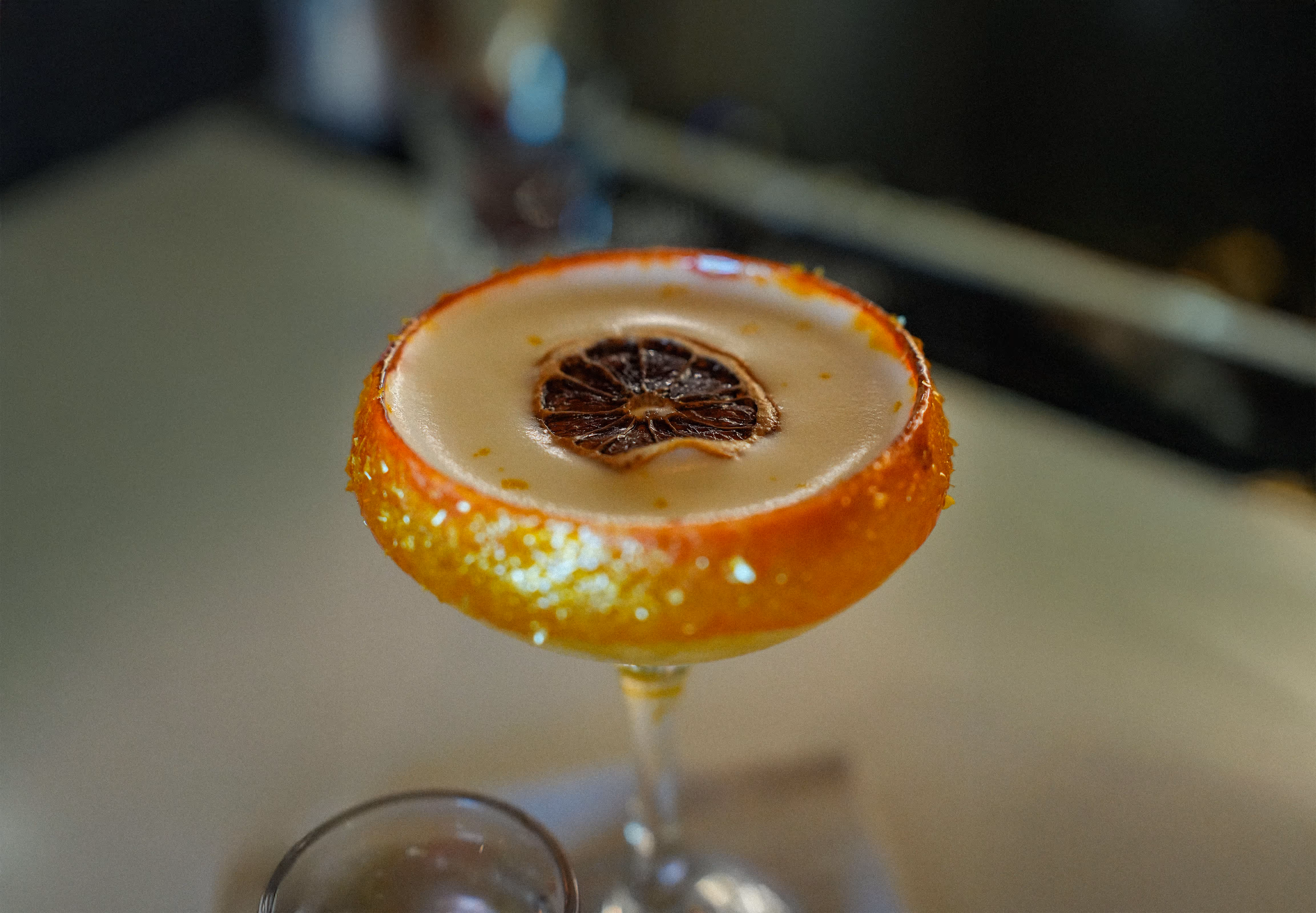 Close-up of a festive citrus cocktail in a sugared glass, garnished with a dried orange slice, a signature drink from Osteria del Mar Miami Beach.