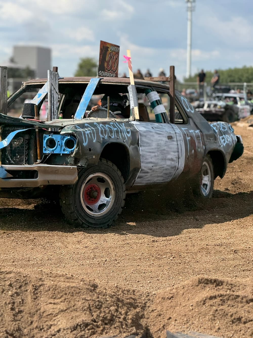 Damaged race car with painted graffiti on a dirt track during a demolition derby event.
