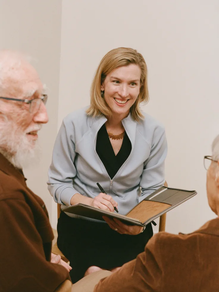 Care manager in gray blazer taking notes while meeting with senior clients.