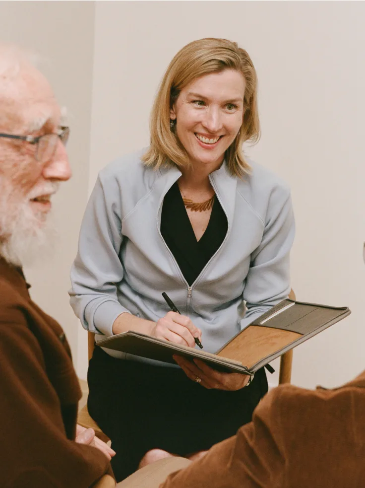 Care manager smiling while taking notes during a consultation with an older adult client.