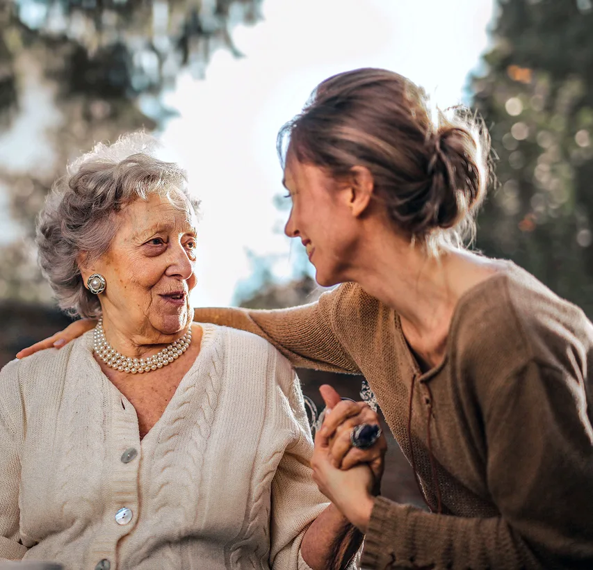 Smiling caregiver with arm around senior woman's shoulder outdoors, demonstrating compassionate in-home care support.