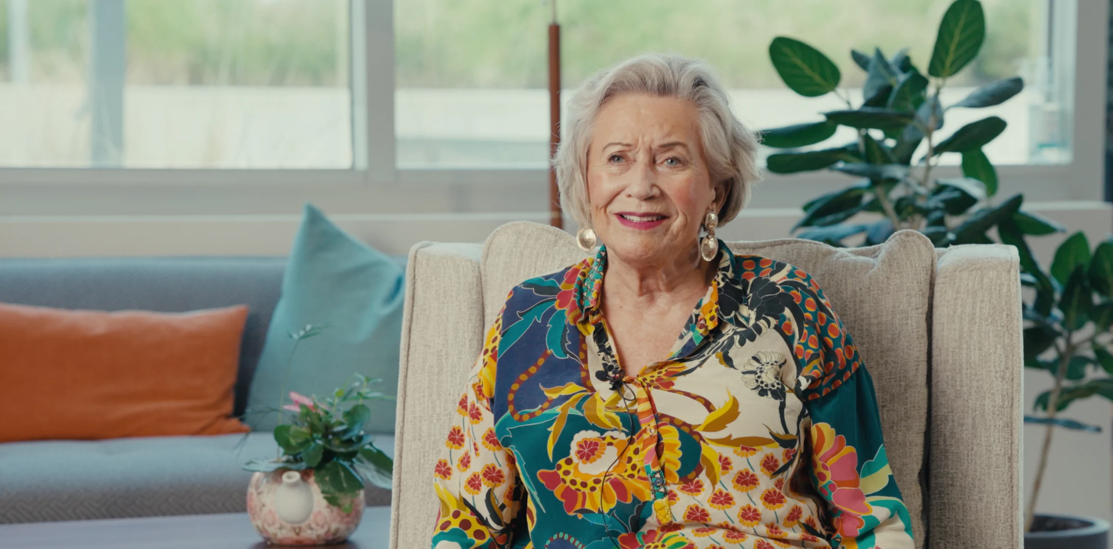 Senior woman with white hair smiling in bright living room with plants and natural light