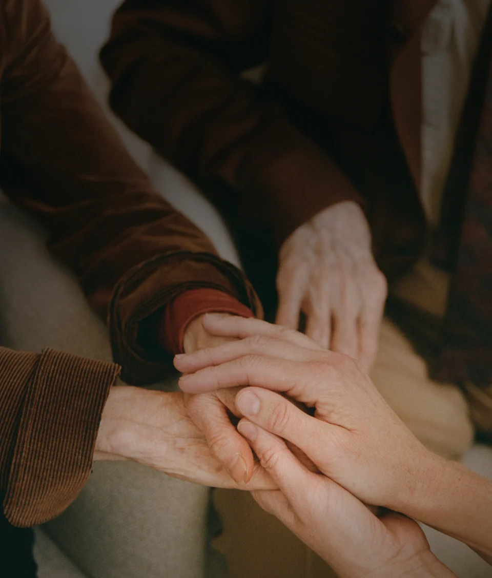 Multiple hands stacked together in a circle, showing care and support among family or caregivers.
