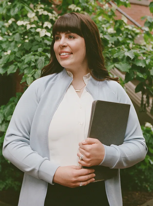 Smiling care manager holding tablet with ivy-covered brick wall backdrop.