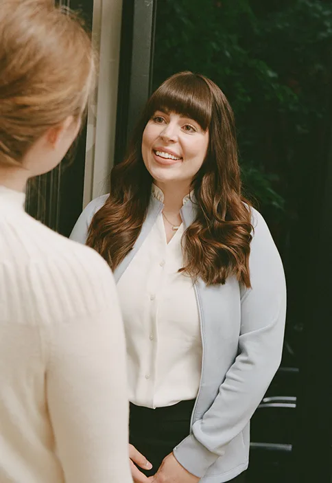 Smiling caregiver in white blouse speaking with client at home, demonstrating compassionate aging-in-place support.