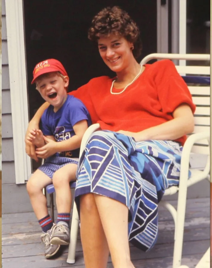 Woman and young boy laughing together on porch chair, representing family-centered care and intergenerational connection.