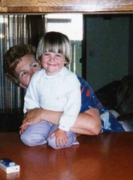 Adult holding smiling toddler at wooden table, depicting multi-generational family care and bonding.