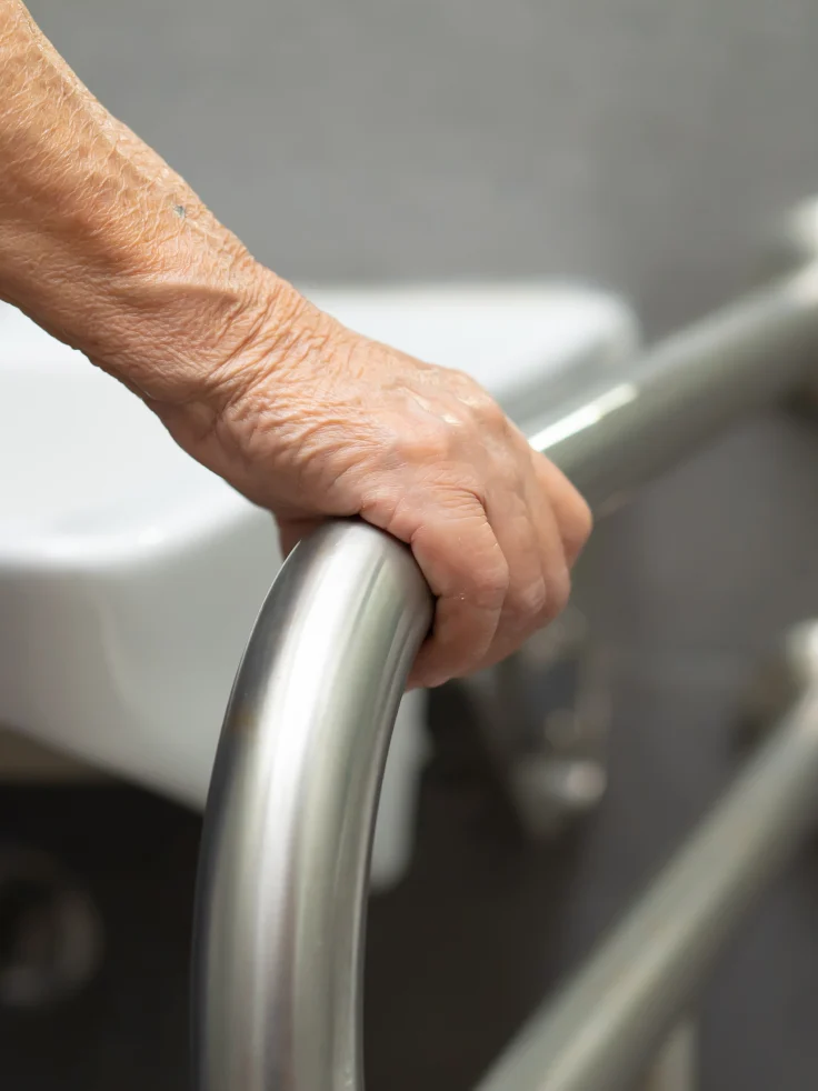 Senior's hand gripping bathroom safety rail for stability and mobility support.