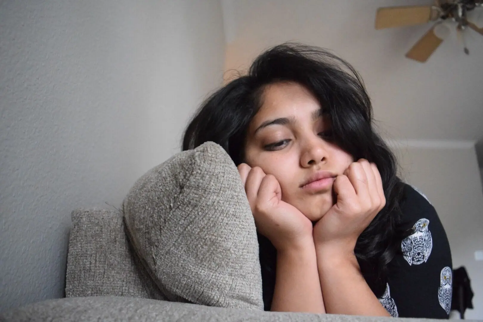 A teenage girl sits on a couch with her head in her hands, appearing sad and upset.