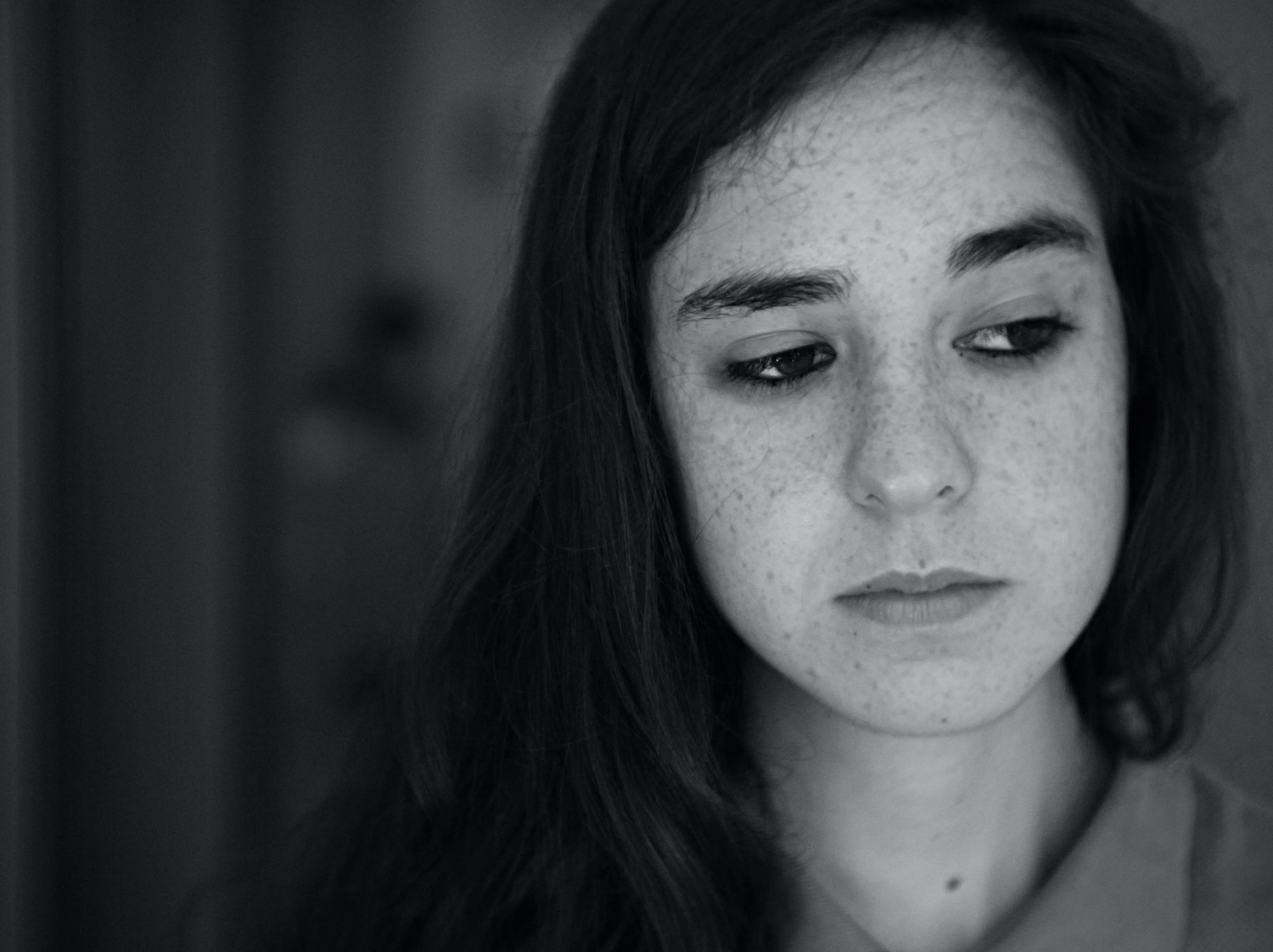 A young woman looks down with a sad, distant expression in a black and white photo.