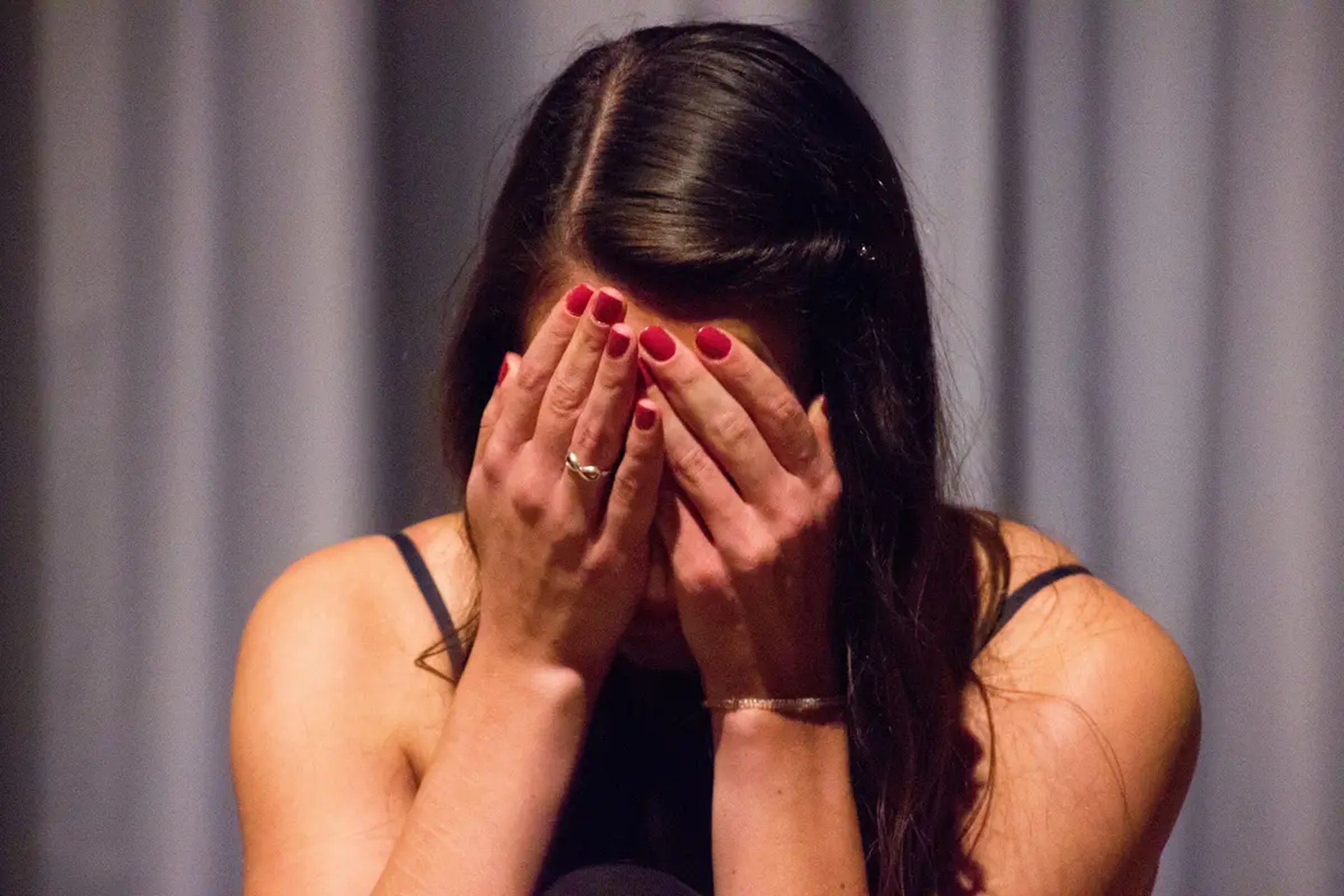 A woman sits with her face buried in her hands, appearing distressed or upset.