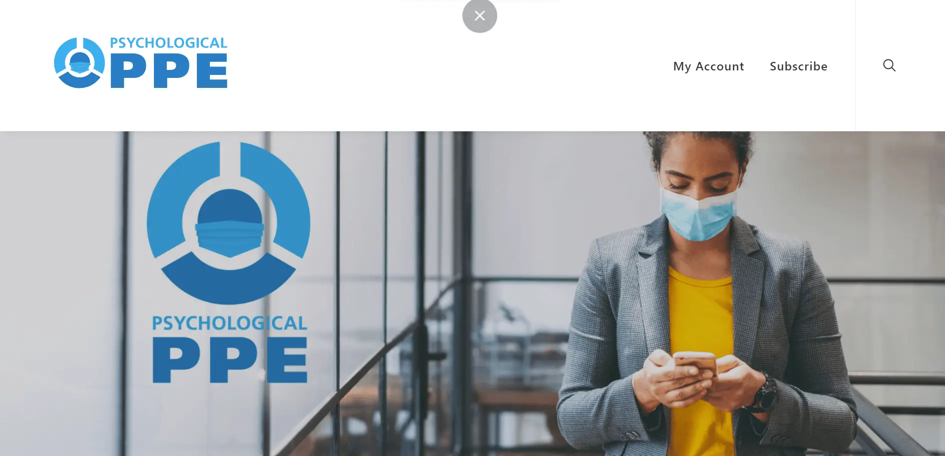 A woman wearing a face mask and business attire looks at her phone while standing indoors beside a logo that reads “Psychological PPE.”