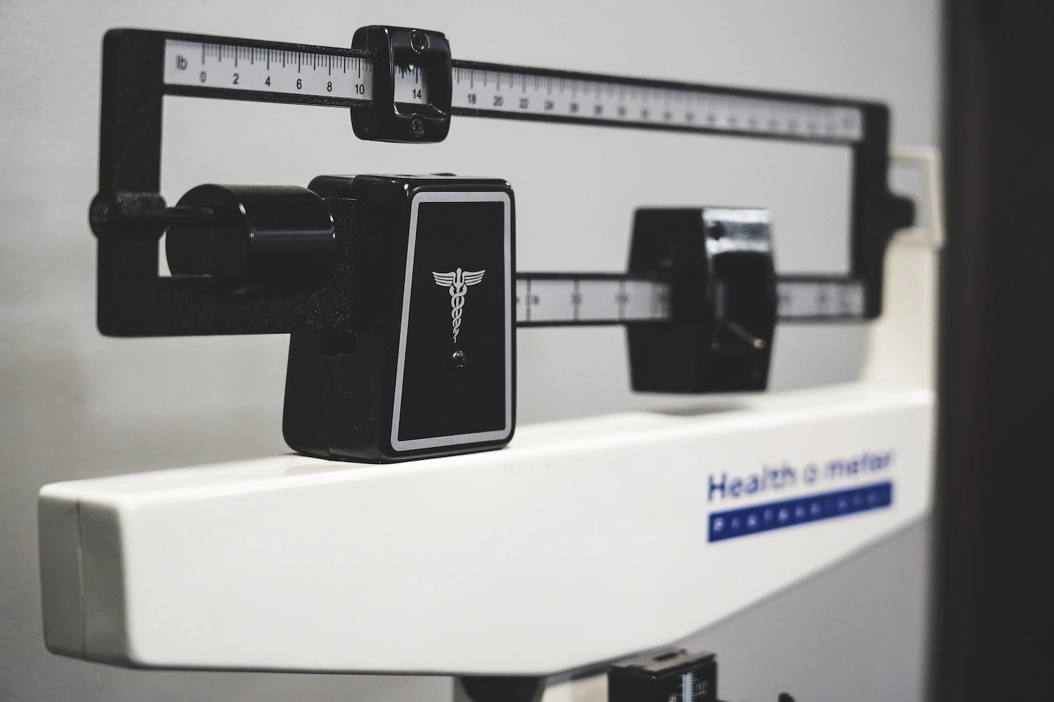 A close-up of a mechanical doctor’s scale used for measuring weight, featuring the caduceus medical symbol and balance sliders.